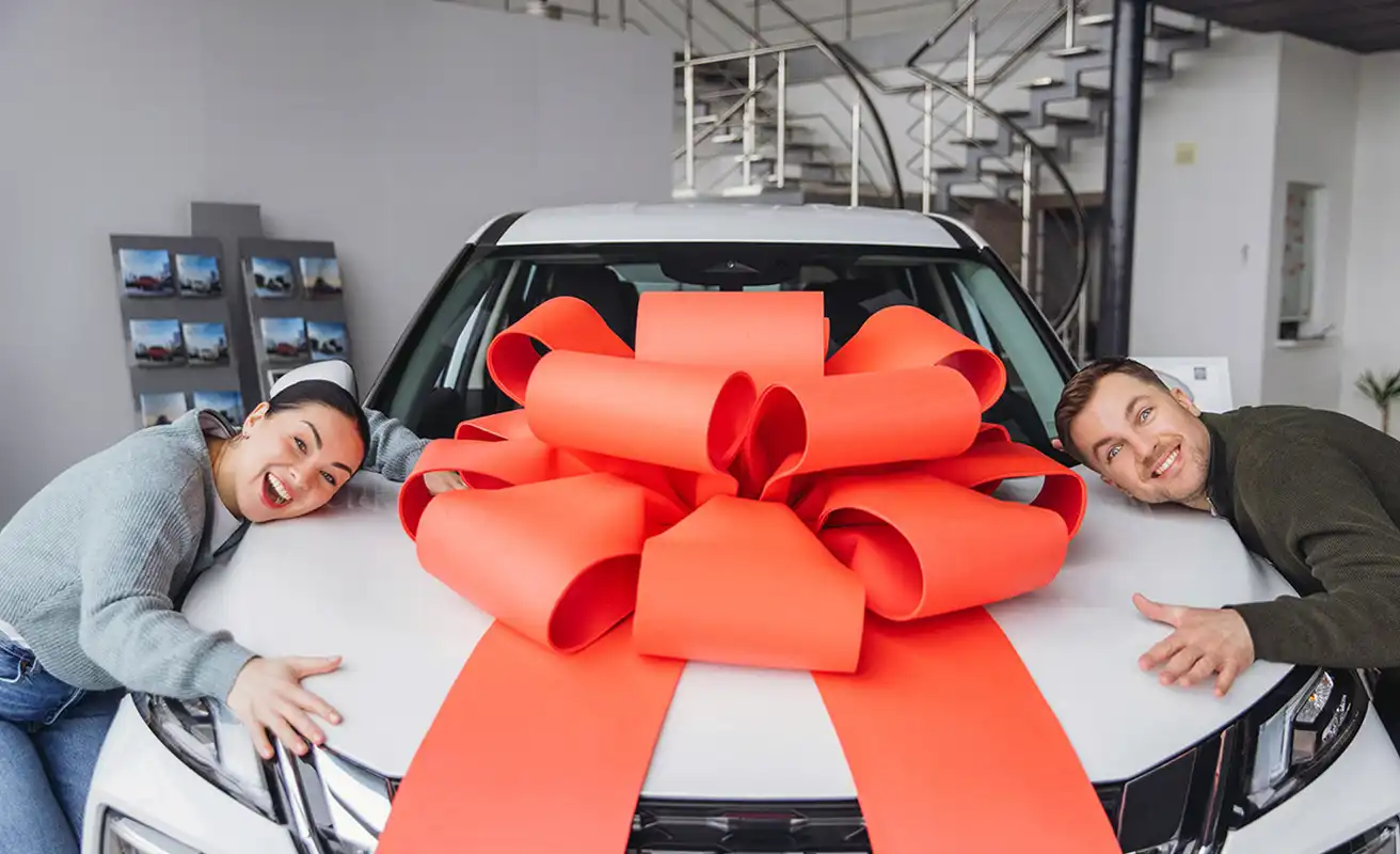 A happy couple with their new SUV wrapped in a red bow